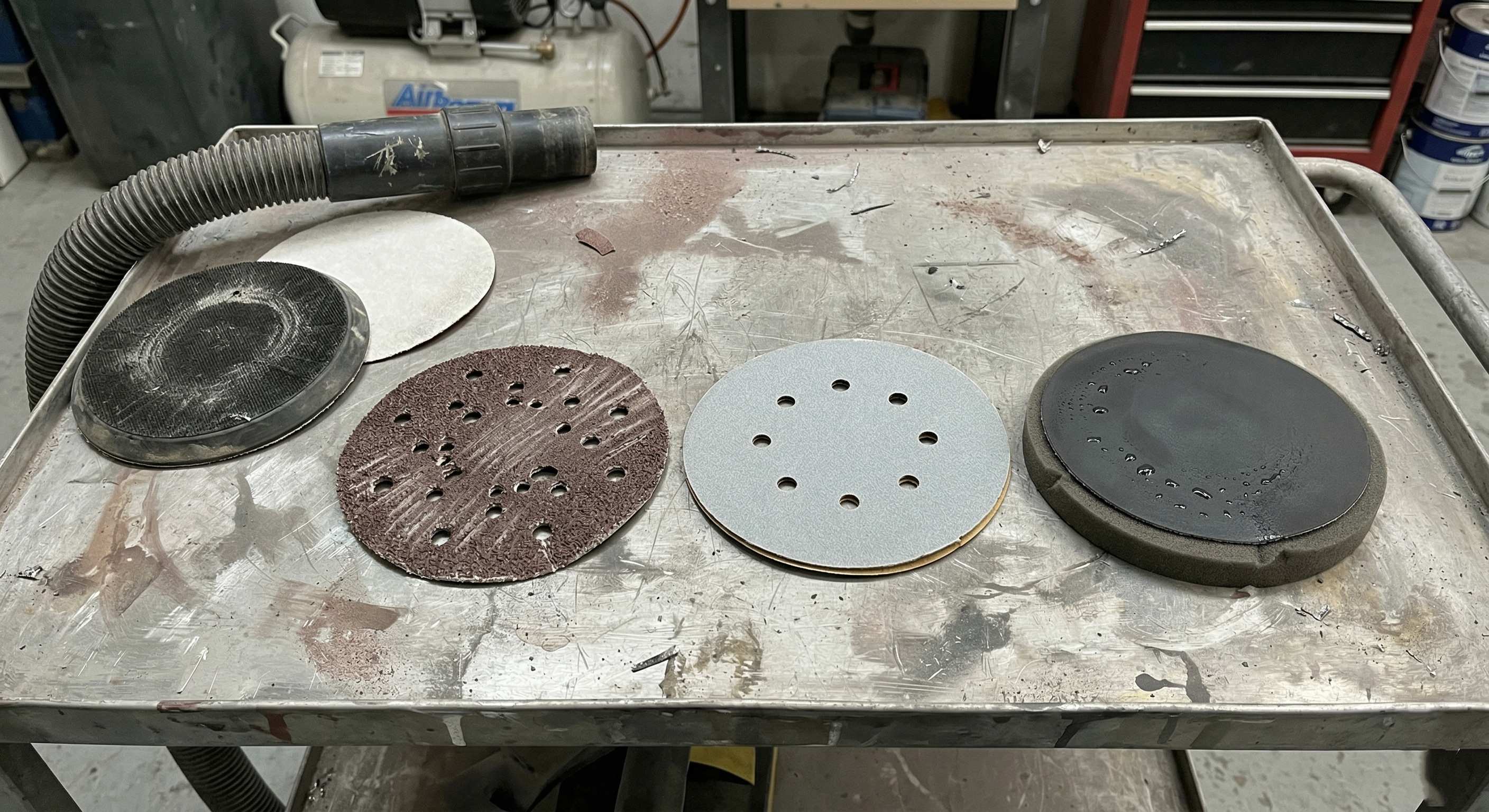Three 150mm sanding disc types on a workshop trolley for automotive refinishing comparison.